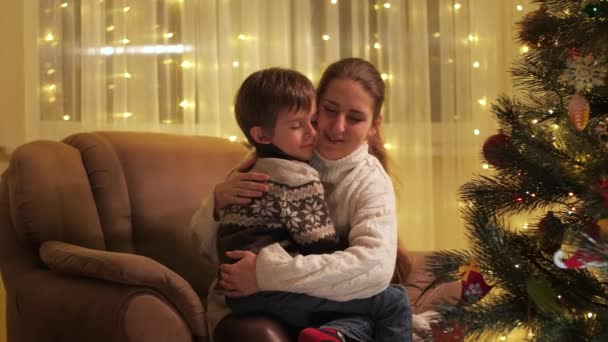 Sevimli çocuk Noel ağacının yanında, koltuğunda annesine sarılıyor. Aileler ve çocuklar kış tatilini kutluyor. — Stok video