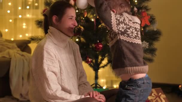 Netter Junge feiert Weihnachten mit seiner Mutter und setzt den Weihnachtsmann auf. Familien und Kinder feiern Winterurlaub. — Stockvideo