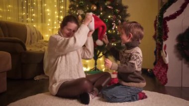 Mutlu bir anne ve oğlu Noel 'i evde kutluyor ve Noel Baba şapkası takıyor. Aileler ve çocuklar kış tatilini kutluyor.