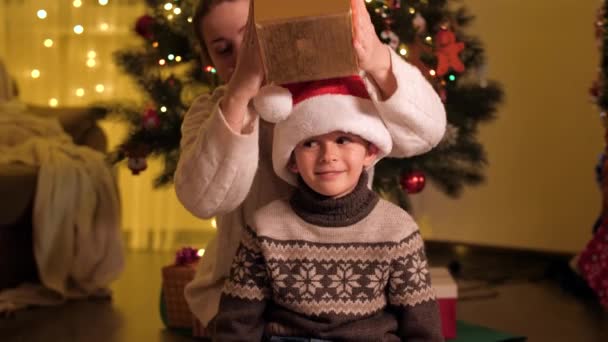 幸せな母は彼女の息子にクリスマスプレゼントを与え、彼を抱きしめる。冬の休日を祝う家族や子供. — ストック動画