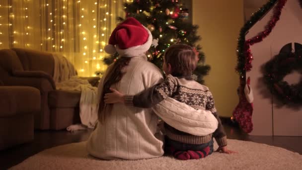 Annesiyle birlikte oturma odasında oturmuş Noel ağacını seyreden küçük bir çocuk. Aileler ve çocuklar kış tatilini kutluyor. — Stok video
