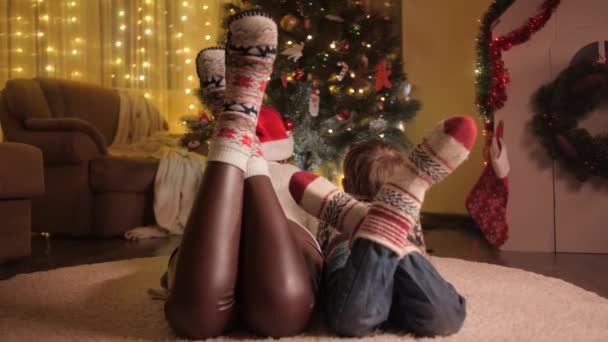 Vista trasera de la familia con calcetines de lana acostados en la alfombra y mirando el brillante árbol de Navidad. Las emociones puras de las familias y los niños que celebran las vacaciones de invierno. — Vídeo de stock