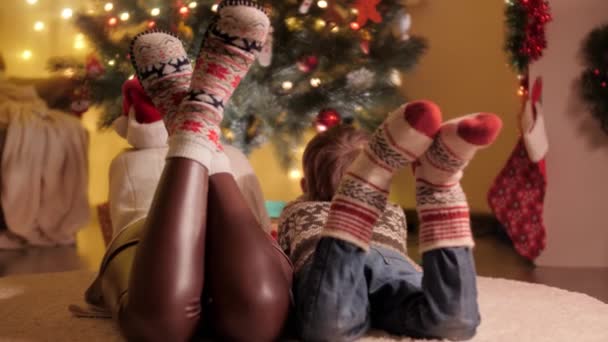 Primer plano de la familia en calcetines de lana de punto que buscan en el árbol de Navidad decorado en la casa. Las emociones puras de las familias y los niños que celebran las vacaciones de invierno. — Vídeos de Stock