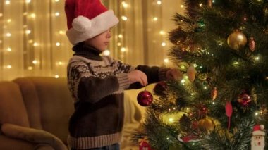 Noel Baba şapkalı küçük çocuk Noel için hazırlanıyor ve Noel ağacı süslüyor. Aile ve çocukların kış tatilini kutladıkları saf duygular..