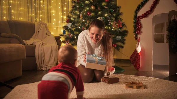 Menino no traje do Papai Noel rastejando até sua mãe sentada debaixo da árvore de Natal. Famílias e crianças comemorando as férias de inverno. — Fotografia de Stock