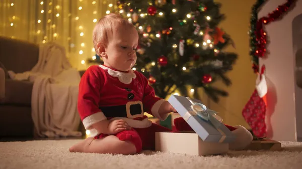 Petit garçon en costume de Père Noël ouvre boîte cadeau de Noël. Familles et enfants célébrant les vacances d'hiver. — Photo