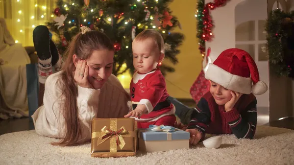 Porträt eines lächelnden Babys mit Bruder und Mutter, die an Weihnachten auf dem Boden liegen. Familien und Kinder feiern Winterurlaub. — Stockfoto