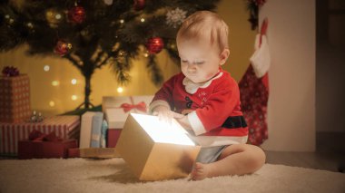 Noel Baba kostümlü şirin erkek bebek hediye kutusunun içine bakıyor. Aileler ve çocuklar kış tatilini kutluyor.
