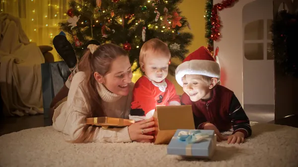 Счастливая смеющаяся семья открывает коробку с подарками на Рождество и заглядывает внутрь. Семьи и дети празднуют зимние праздники. — стоковое фото