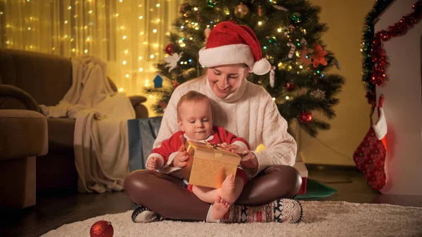 Feliz madre sonriente con el niño pequeño mirando ginside caja de regalo de Navidad. Familias y niños celebrando las vacaciones de invierno. —  Fotos de Stock