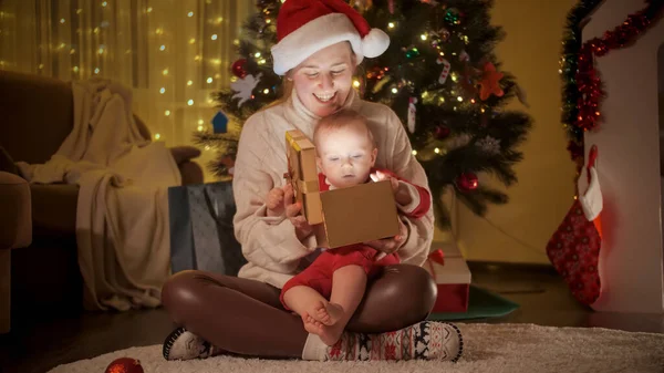 Felice madre ridente con il piccolo bambino in possesso di scatola regalo di Natale e sorridente in macchina fotografica. Famiglie e bambini festeggiano le vacanze invernali. — Foto Stock