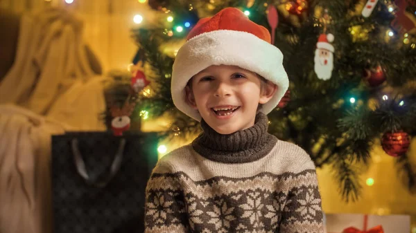 Feliz menino rindo em chapéu de Papai Noel ao lado da árvore de Natal. Famílias e crianças comemorando as férias de inverno. — Fotografia de Stock