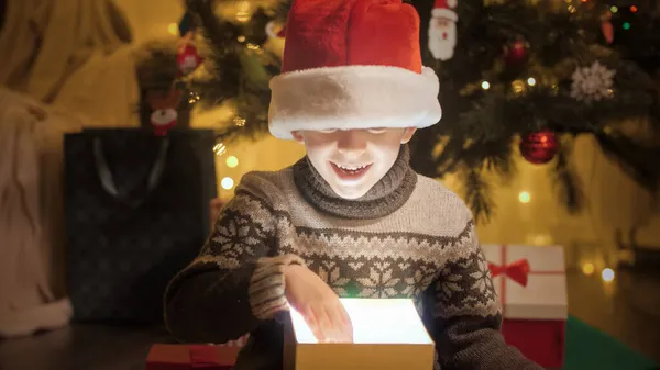 Feliz niño sonriente tomando Chrsitmas regalo de brillante caja de regalo mágico bajo el árbol de Navidad — Foto de Stock