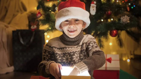 Portrét veselého usměvavého chlapce ve svetru a Santa klobouk rozbalování vánoční dárky a otevření dárkové krabice — Stock fotografie