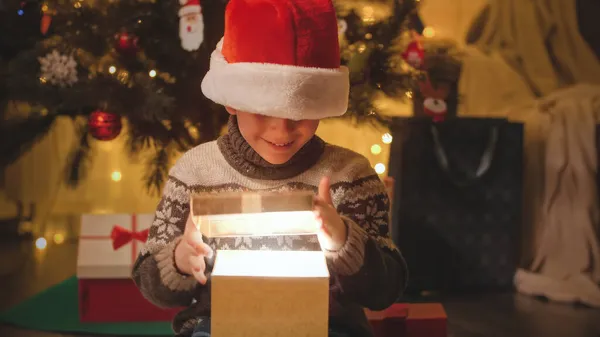 Portret wesołego chłopca trzymającego prezent świąteczny i zaglądającego do pudełka. Rodziny i dzieci świętujące ferie zimowe. — Zdjęcie stockowe