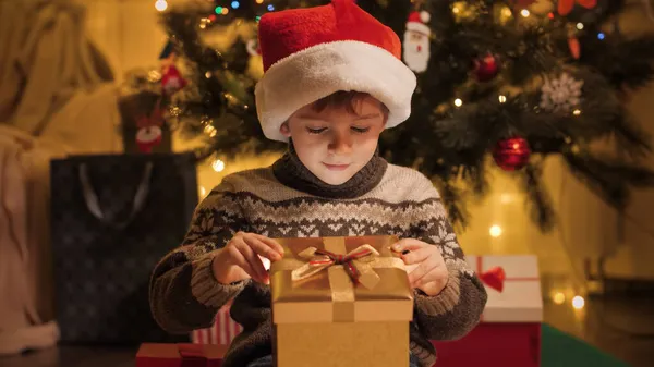 Porträt eines erstaunten und aufgeregten Jungen mit Weihnachtsmütze, der in die Weihnachtsgeschenkschachtel schaut. Familien und Kinder feiern Winterurlaub. — Stockfoto