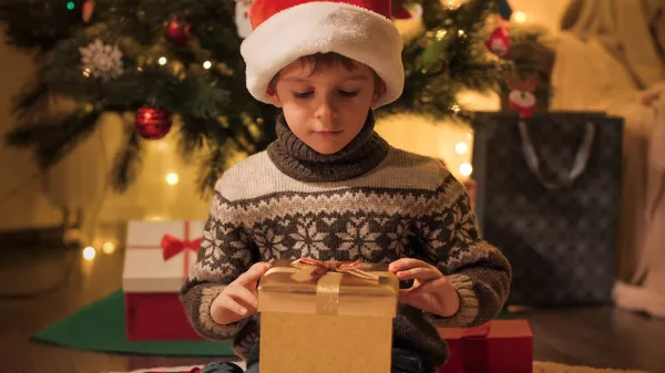 Garçon mignon dans le chapeau de Père Noël regardant à l'intérieur boîte cadeau de Noël. Magie des vacances de Noël. Familles et enfants célébrant les vacances d'hiver. — Photo