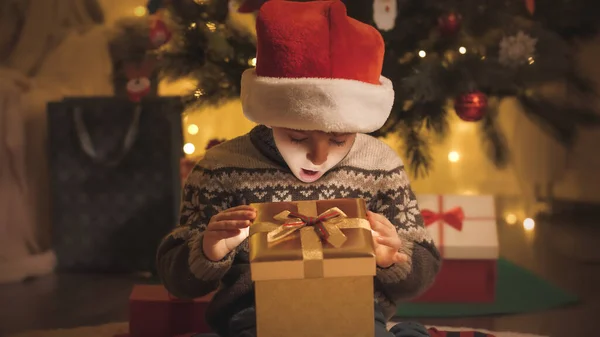 Τονισμένο πορτρέτο του έκπληκτου αγοριού κοιτάζοντας μέσα λαμπερό χριστουγεννιάτικο δώρο κουτί τη νύχτα — Φωτογραφία Αρχείου