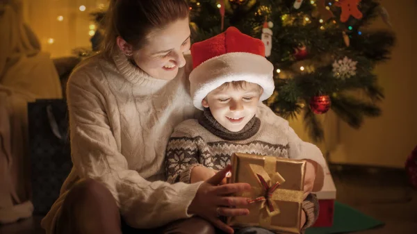 魔法のクリスマスプレゼントボックスの中を見て息子と幸せな母親。冬の休日を祝う家族や子供. — ストック写真