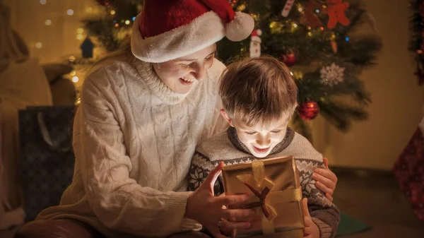 Garoto sorridente alegre com a mãe desembrulhando e olhando dentro da caixa com presentes de Natal e presentes. Famílias e crianças comemorando as férias de inverno. — Fotografia de Stock