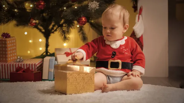 Χαριτωμένο αγοράκι ξετυλίγεται και ψάχνει μέσα στο κουτί δώρου των Χριστουγέννων κάτω από διακοσμημένο χριστουγεννιάτικο δέντρο. Οικογένειες και παιδιά γιορτάζουν χειμερινές διακοπές. — Φωτογραφία Αρχείου