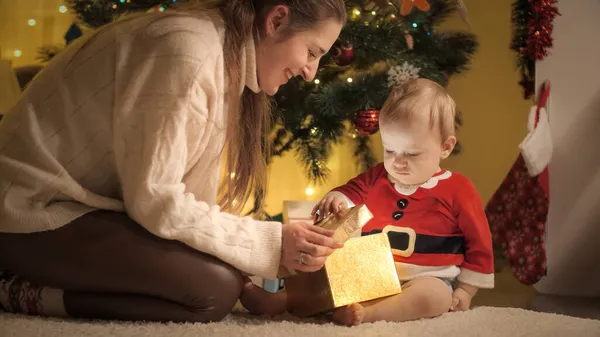 Feliz madre dando regalo de Navidad en caja de oro a su pequeño hijo. Familias y niños celebrando las vacaciones de invierno. —  Fotos de Stock