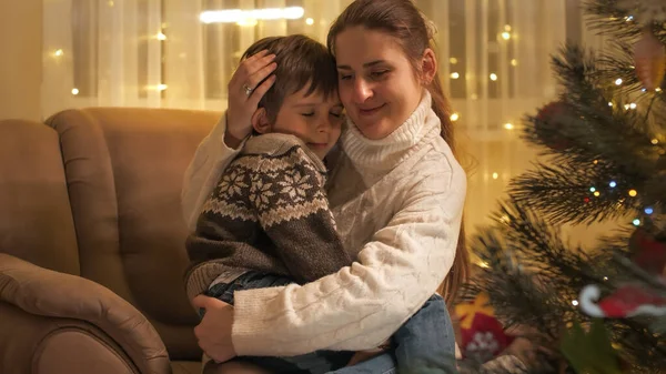 Souriant jeune mère étreignant son fils assis dans un fauteuil à côté de l'arbre de Noël dans le salon. Familles et enfants célébrant les vacances d'hiver. — Photo