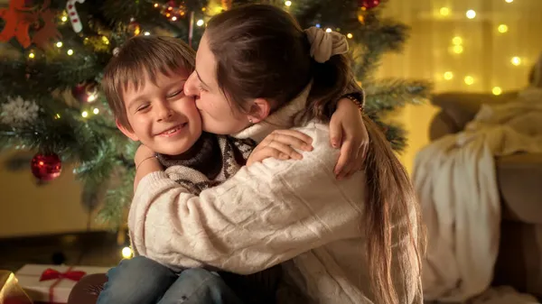 Retrato de madre feliz besando a su hijo sonriente en la mejilla mientras celebra la Navidad o Año Nuevo —  Fotos de Stock