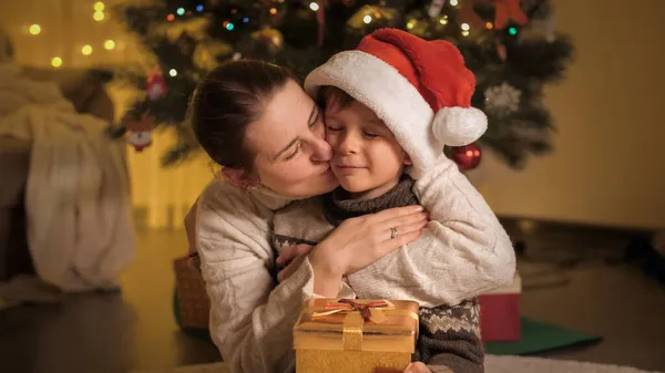 Porträtt av leende mor krama och kyssa sin son efter att ha gett honom julklapp i gyllene presentförpackning — Stockfoto