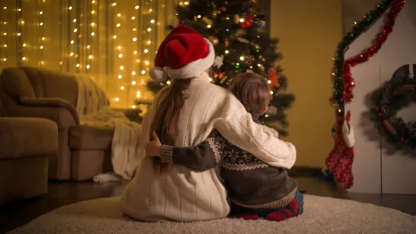 Vue arrière de la mère et du fils assis dans le salon et regardant les lumières colorées de l'arbre de Noël. Familles et enfants célébrant les vacances d'hiver. — Photo