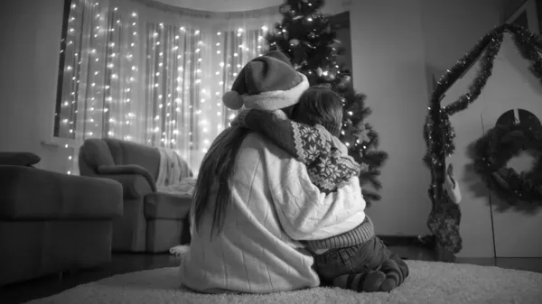 Svart adn vit bild av mor med liten son kramas och titta på vackra julgran hemma — Stockfoto
