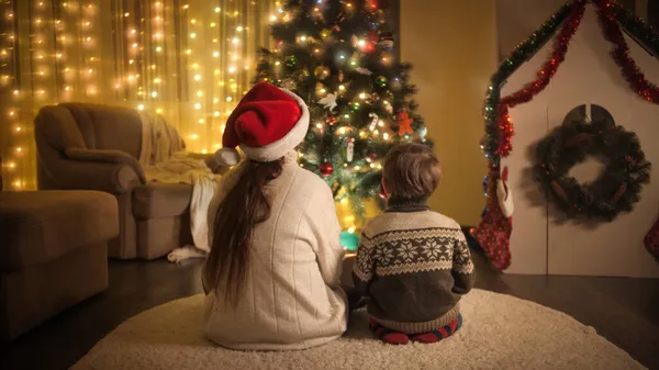 Bakifrån av lycklig familj sitter på golvet och tittar på färgglada julgran ljus. Familjer och barn som firar vinterlov. — Stockfoto