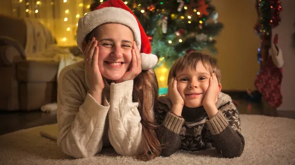 Portré boldog fiú anyával feküdt a nappaliban díszített karácsonyra és mosolygott a kamera előtt. A téli ünnepeket ünneplő családok és gyermekek. — Stock Fotó