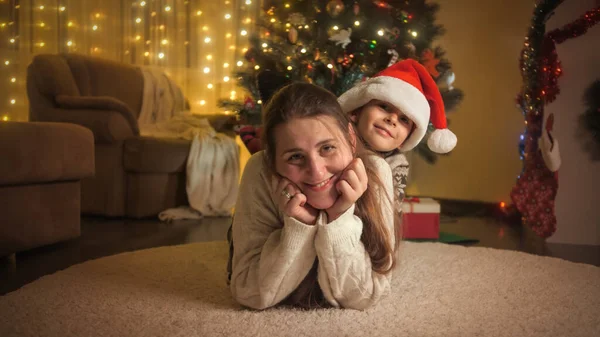 母を持つ幸せな少年の肖像画が床に横たわっており、クリスマスツリーの横に楽しみを持っています。冬の休日を祝う家族や子供. — ストック写真