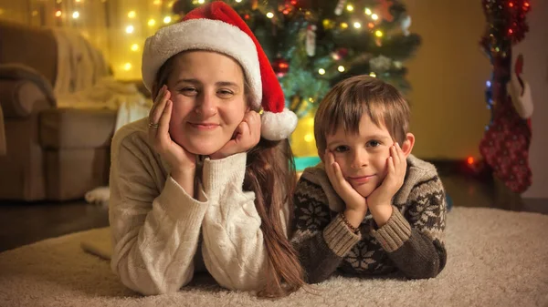 Lächelnder Junge mit Mutter, die auf dem Teppich unter dem Weihnachtsbaum liegt, während sie Neujahr feiert. Familien und Kinder feiern Winterurlaub. — Stockfoto