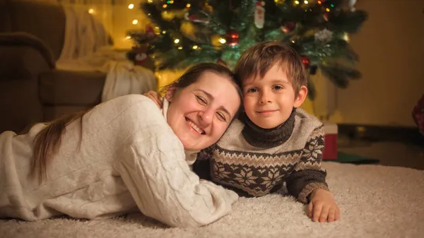 Oğluyla gülümseyen anne portresi. Oturma odasındaki Noel ağacının altında, halıya sarılıp yatıyor. Aile ve çocukların kış tatilini kutladıkları saf duygular..