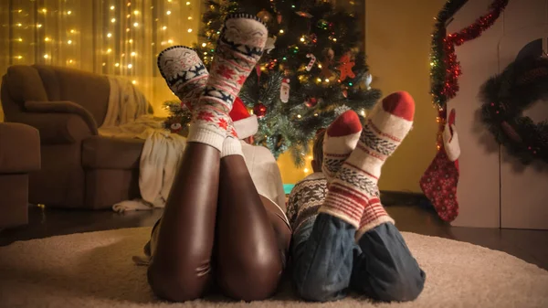 Visão traseira da família vestindo meias de lã deitado no tapete e olhando para a árvore de Natal brilhante. Emoções puras de famílias e crianças que celebram férias de inverno. — Fotografia de Stock