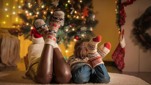 Primo piano dei piedi della famiglia in calzini di lana lavorati a maglia che giacciono accanto all'albero di Natale incandescente in soggiorno. Emozioni pure di famiglie e bambini che festeggiano vacanze invernali. — Foto Stock