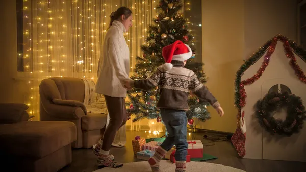 Mãe feliz com filho dançando aroung brilhante árvore de Natal na sala de estar. Emoções puras de famílias e crianças que celebram férias de inverno. — Fotografia de Stock
