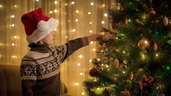 Liten pojke i Santa mössa dekorera julgran med leksaker och grannlåt. Rena känslor hos familjer och barn som firar vinterlov. — Stockfoto