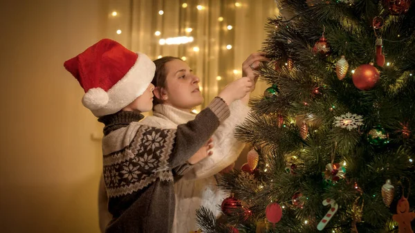 Leende mor med liten son dekorera julgran med leksaker och grannlåt. Rena känslor hos familjer och barn som firar vinterlov. — Stockfoto