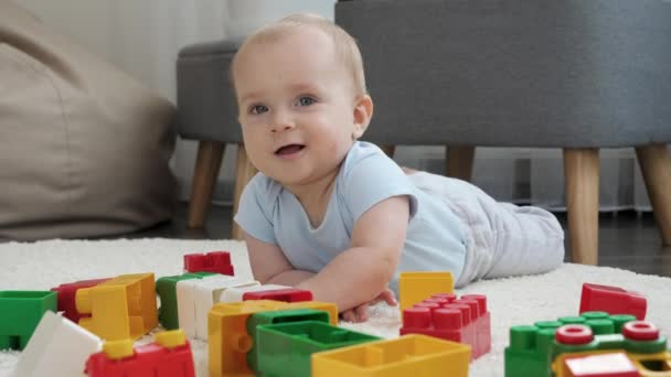 Retrato de niño sonriente alegre jugando con ladrillos de colores y bloques en el suelo en la sala de estar. Concepto de desarrollo infantil, educación y creatividad en el hogar — Vídeos de Stock