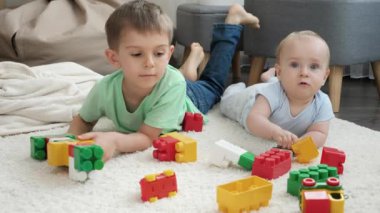 Küçük kardeşi olan mutlu çocuk renkli oyuncak tuğlalardan ve bloklardan ev inşa ediyor. Çocuk gelişimi, eğitim ve yaratıcılık kavramı