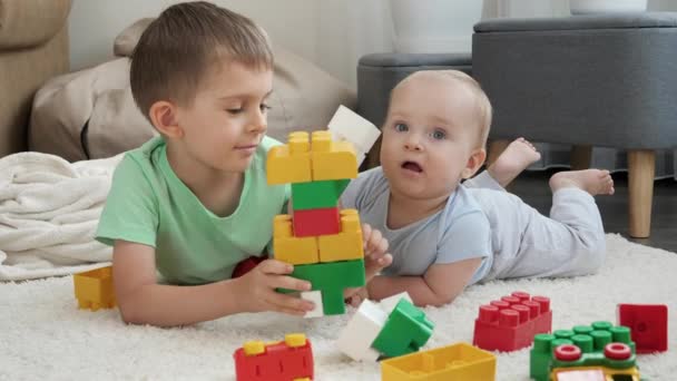 Chłopiec uczy młodszego brata budować wieżę z klocków i cegieł. Koncepcja rozwoju, edukacji i kreatywności dzieci w domu — Wideo stockowe