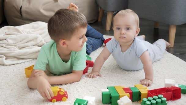 Feliz niño sonriente con hermano mayor jugando juguetes en la alfombra en la sala de estar. Concepto de desarrollo infantil, educación y creatividad en el hogar — Vídeos de Stock