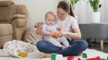 Genç, gülümseyen bir anne kucağında küçük oğluyla oturma odasında oyuncak arabalarla oynuyor. Ailenin birlikte zaman geçirmesi ve çocuk gelişimi kavramı