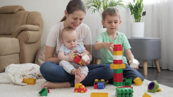 Lächelnd baut eine glückliche Familie einen hohen Turm mit Spielzeugklötzen und Ziegeln. Konzept der gemeinsamen Zeit der Familie und der Entwicklung der Kinder — Stockvideo