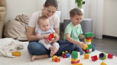 Anneleri halının üzerinde oynayan ve oyuncak kulesi inşa eden mutlu çocuklar. Ailenin birlikte zaman geçirmesi ve çocuk gelişimi kavramı