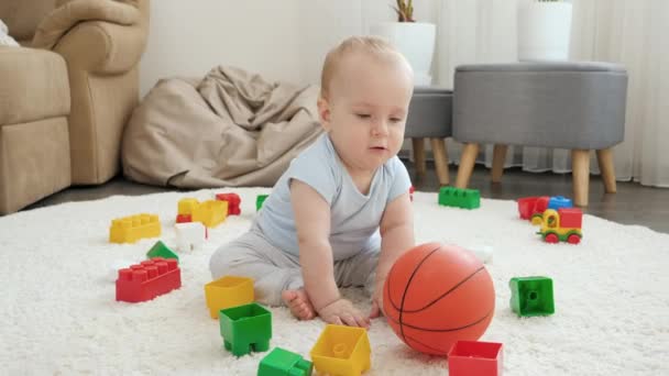 Niño pequeño rodando y golpeando la pelota de baloncesto en la alfombra en casa. Concepto de desarrollo infantil, deportes, educación y creatividad en el hogar — Vídeos de Stock