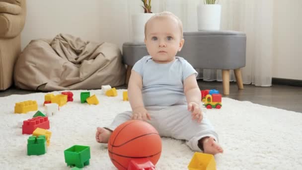 Χαρούμενο χαμογελαστό αγοράκι που παίζει μπάσκετ με τους γονείς του στο χαλί στο σπίτι. Έννοια της ανάπτυξης των παιδιών, του αθλητισμού, της εκπαίδευσης και της δημιουργικότητας στο σπίτι — Αρχείο Βίντεο